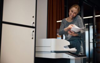 Smiling businesswoman talks on the phone collecting outputs from a multifunction printer