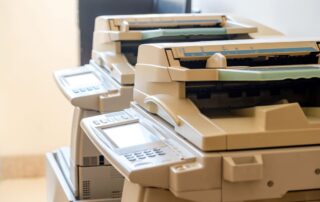 A close-up view of a line of high-end office copiers with document feeders and control panels, illustrating options for businesses considering a copier lease, against a soft beige wall.
