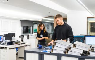 Office employees managing documents and binders in a well-organized workspace, with printers and computers in the background, representing efficient print management solutions.